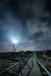 Diminishing perspective of boardwalk against cloudy sky at night