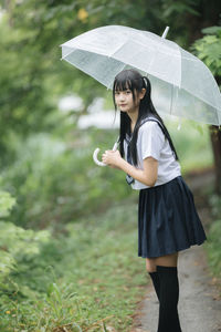 Young student with umbrella standing in park