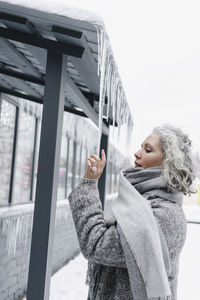 Woman in gray warm clothing touching frozen icicles