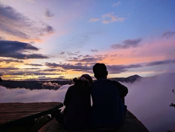 Rear view of men on mountain against sky during sunset