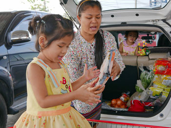 Girl with mother putting groceries in car trunk