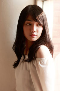 Close-up portrait of young woman standing against gray background