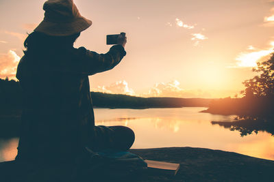 Man photographing sea against sky during sunset