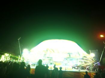 People in illuminated amusement park against sky at night