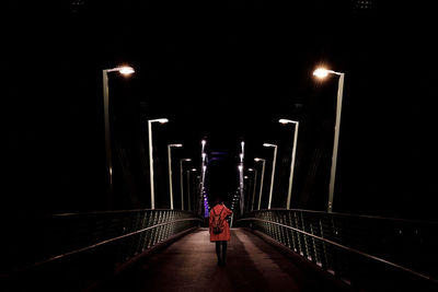 Rear view of man walking on illuminated bridge at night