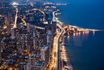 High angle view of illuminated city by lake at night