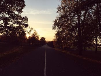 Empty road by trees against sky