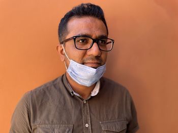 Portrait of young man wearing eyeglasses against orange background