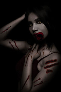 Close-up portrait of spooky young woman holding red rose against black background