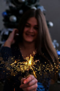 Happy young woman sitting with glass of champagne and bengal light next to the christmas tree. new 