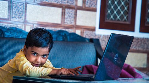 School girl using laptop wearing earphones smiling to camera learning online at home, internet and r