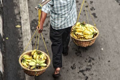 Low section of man holding banana in baskets while walking on road