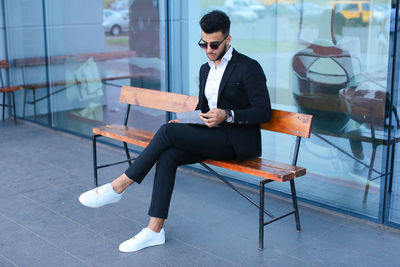 Young businessman using digital tablet sitting on bench outdoors