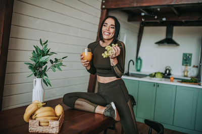 Portrait of smiling woman holding juice sitting at home