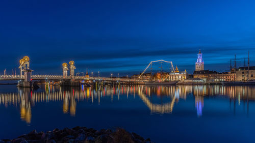 Illuminated city by river against sky at night