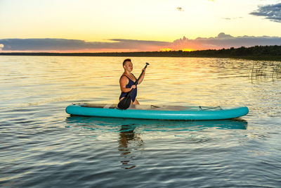 Rear view of man swimming in sea against sky during sunset