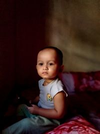 Portrait of cute girl sitting on bed at home