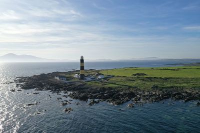 Lighthouse amidst sea and buildings against sky