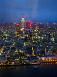 Illuminated buildings by river against sky in city at night