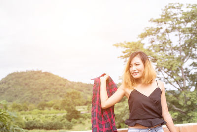 Young woman smiling against sky