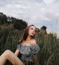 Beautiful young woman looking away while relaxing on land against sky
