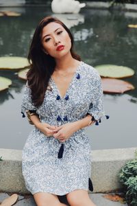 Portrait of young woman sitting on retaining wall against lake in park