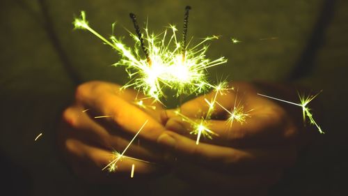 Midsection of person holding lit sparklers at night