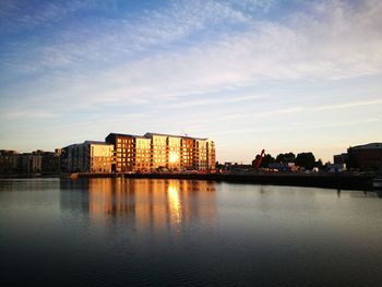 Buildings by river against sky at sunset