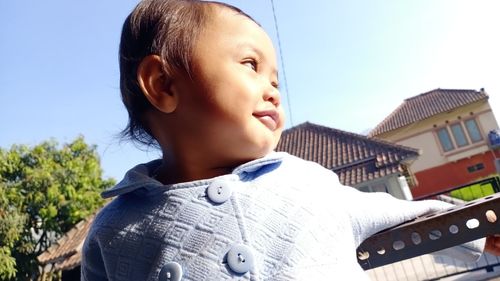 Low angle view of baby boy looking away against sky