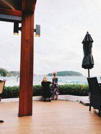 Rear view of people sitting on wood against sky