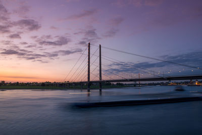 Long exposure of a bridge over river against sky during sunset with passing barge