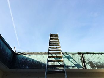 Low angle view of metallic ladder leaning on retaining wall against sky