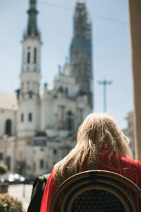 Rear view of woman sitting on chair against church in city during sunny day