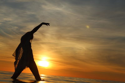 Silhouette person in sea against sky during sunset