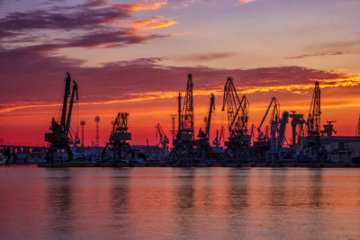 Cranes at commercial dock against sky during sunset