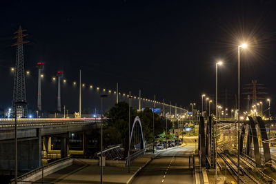 Illuminated street lights by bridge against sky at night