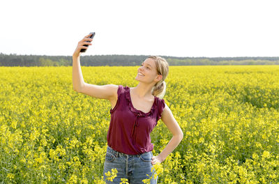 Smiling woman taking selfie while standing amidst oilseed rape