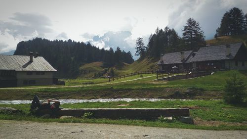 People sitting on house by trees against sky