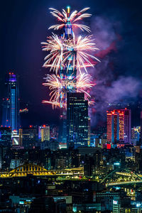 Firework display in city against sky at night