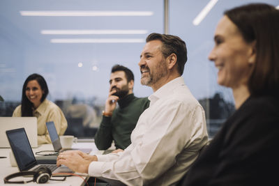 Smiling businessman discussing with male and female colleagues during meeting at office