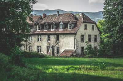 Old building by trees on field against sky