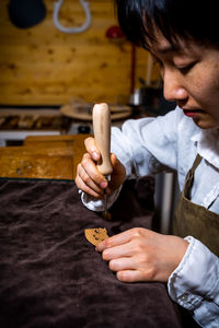 Young chinese woman violin maker signs the jumper of her violin with fire her name in the workshop