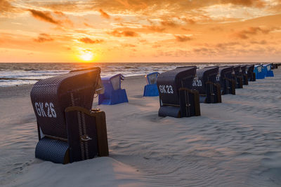 Hooded chairs at beach during sunset