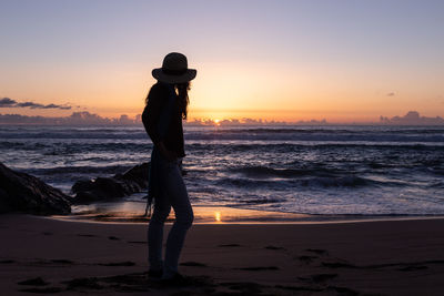 Silhouette woman standing at beach during sunset