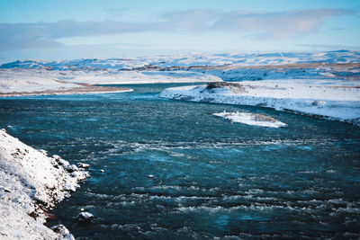 Scenic view of snowcapped landscape by sea against sky