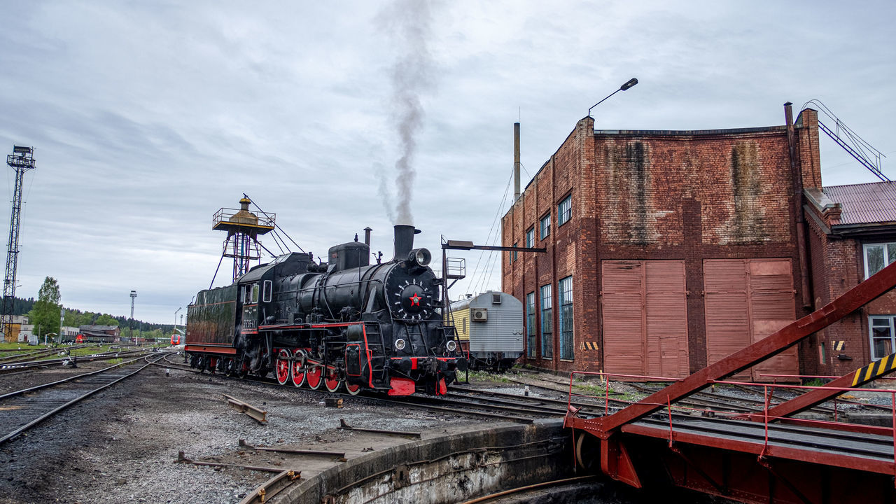 rail transportation, track, train, railroad track, train - vehicle, mode of transportation, transportation, sky, architecture, steam train, smoke - physical structure, cloud - sky, public transportation, built structure, nature, building exterior, locomotive, day, outdoors, no people, shunting yard, pollution, air pollution, railroad car