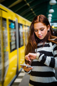 Young woman using phone while standing at railroad station