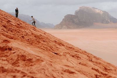 Side view of couple of travelers walking on sandy hill in wadi rum sandstone valley while enjoying freedom and vacation in jordan