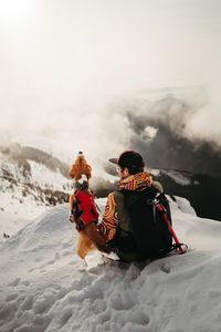 Rear view of man with dog sitting on snow covered landscape