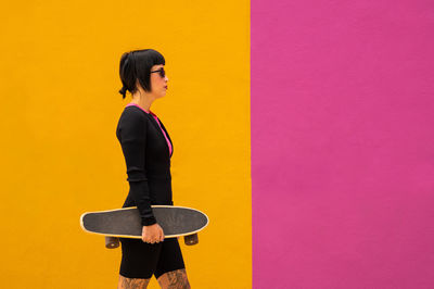 Beautiful woman with short hair posing with a skateboard on a colored background